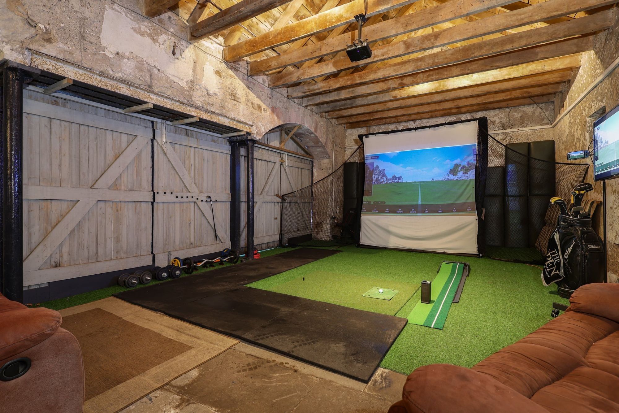 Golf simulator screen and putting strip under the barn's exposed roof timbers