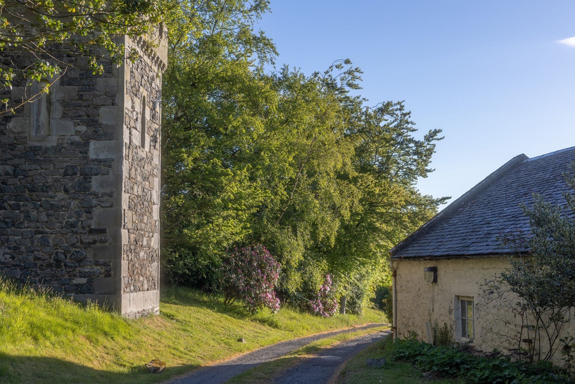 The stone folly tower beside the lane, with the old stone bothy and mature trees