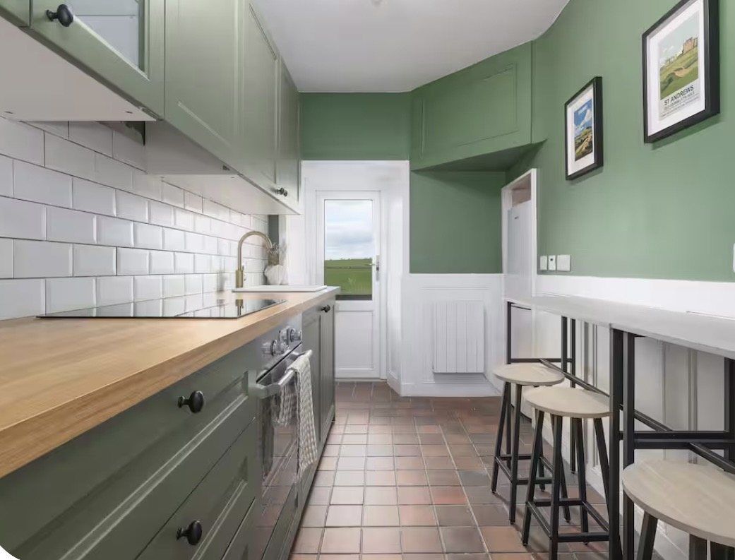 Green shaker kitchen with oak worktops and a breakfast bar at Gardener's Cottage