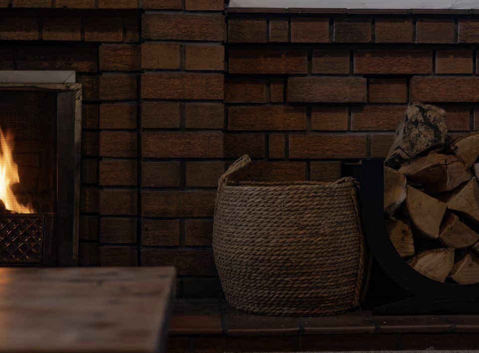 A lit fire in the brick fireplace with a log basket alongside