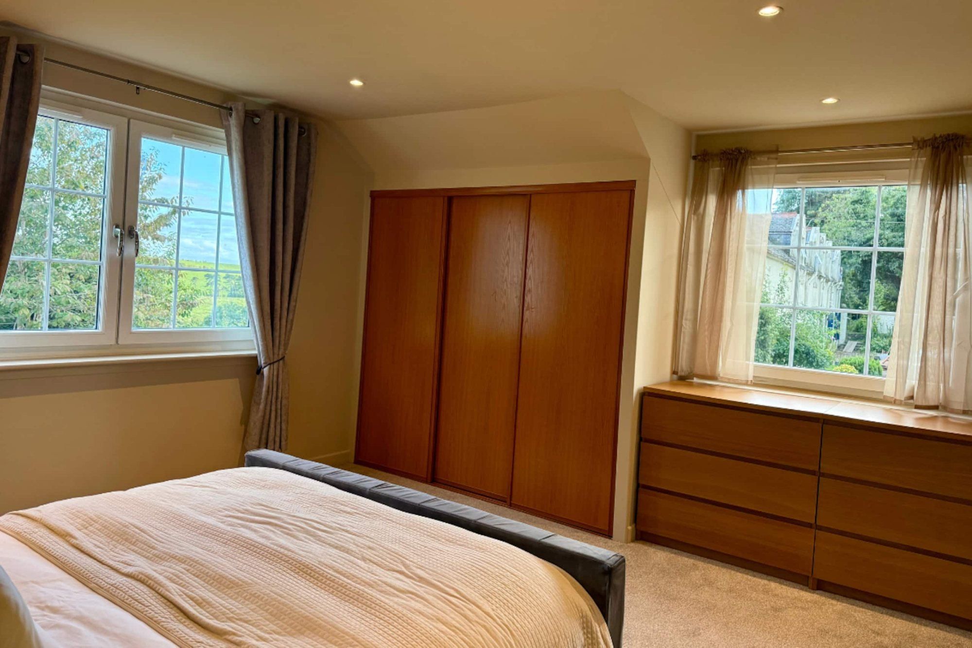 Bedroom with timber wardrobes and windows on two sides looking out to the trees