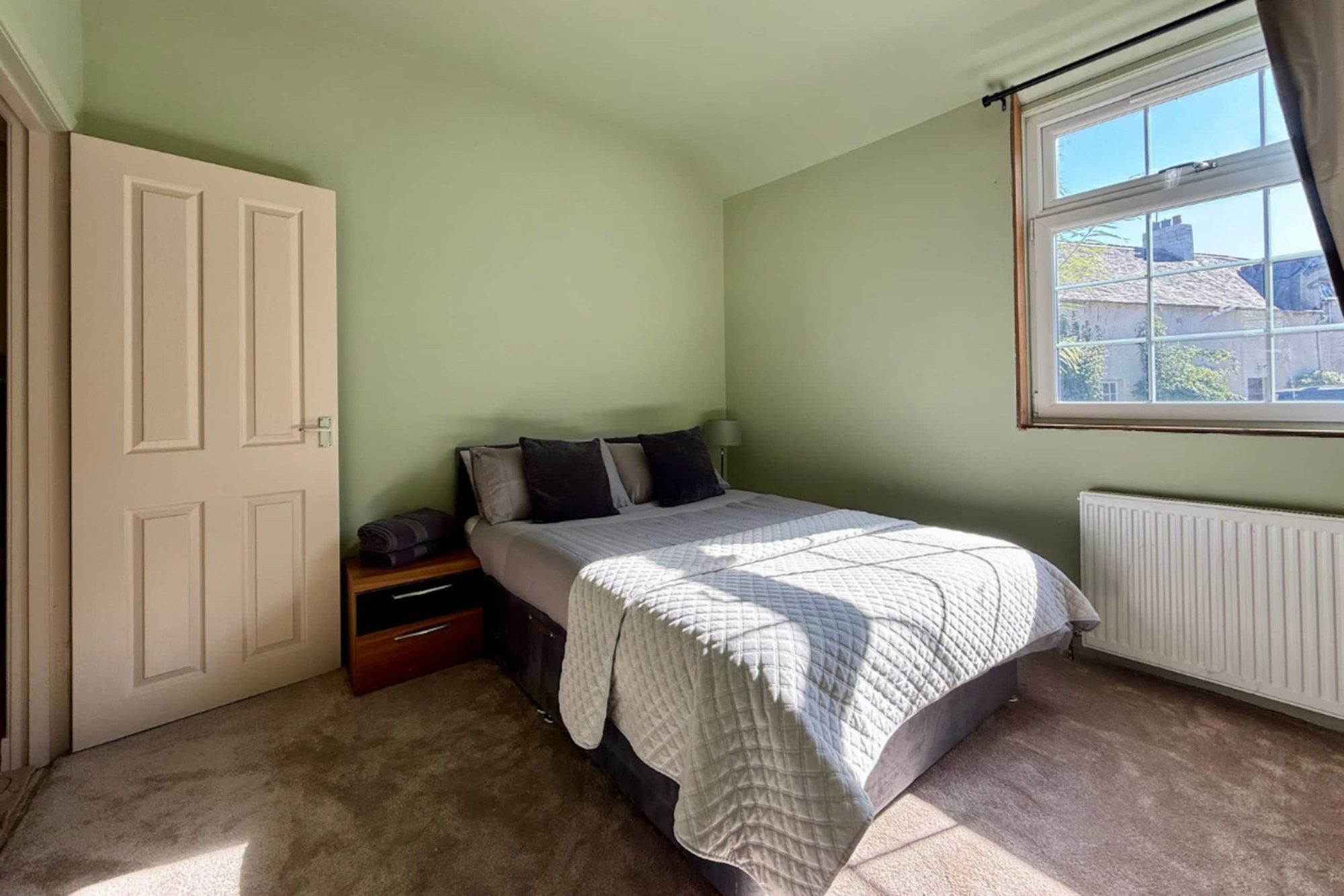Sage-green double bedroom with a window looking across the courtyard