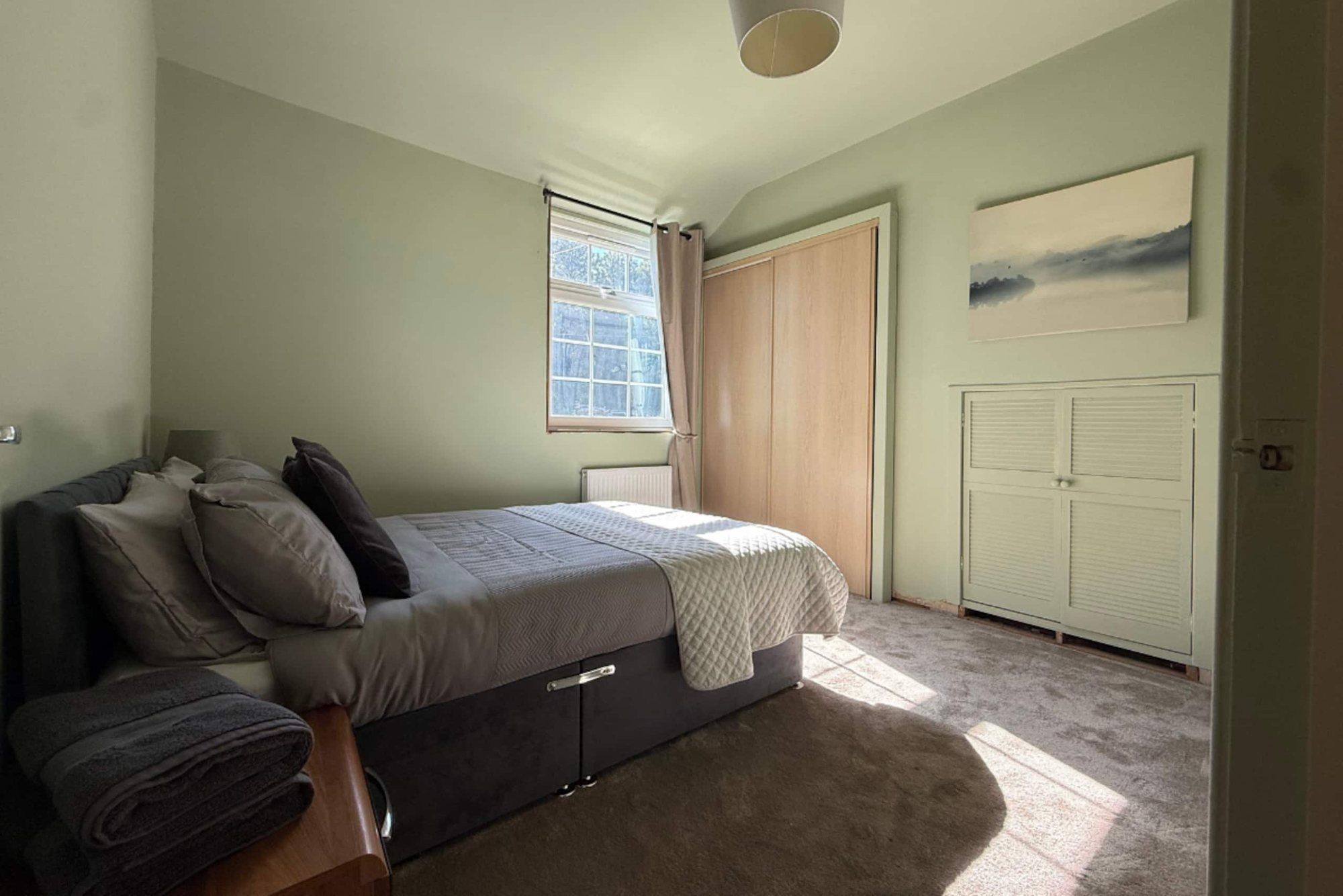 Green bedroom with grey bedding, built-in wardrobes and a cream cupboard