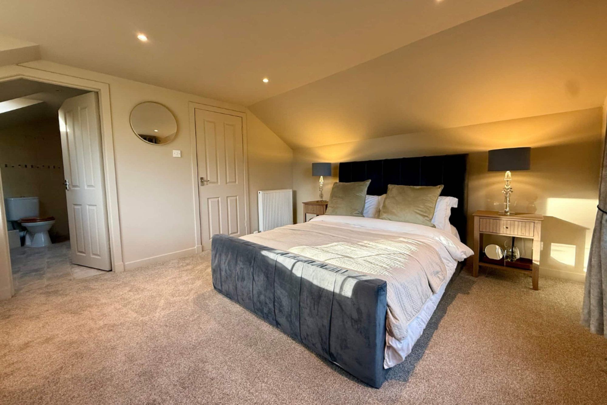 King bedroom with warm lamps and a door through to the en-suite