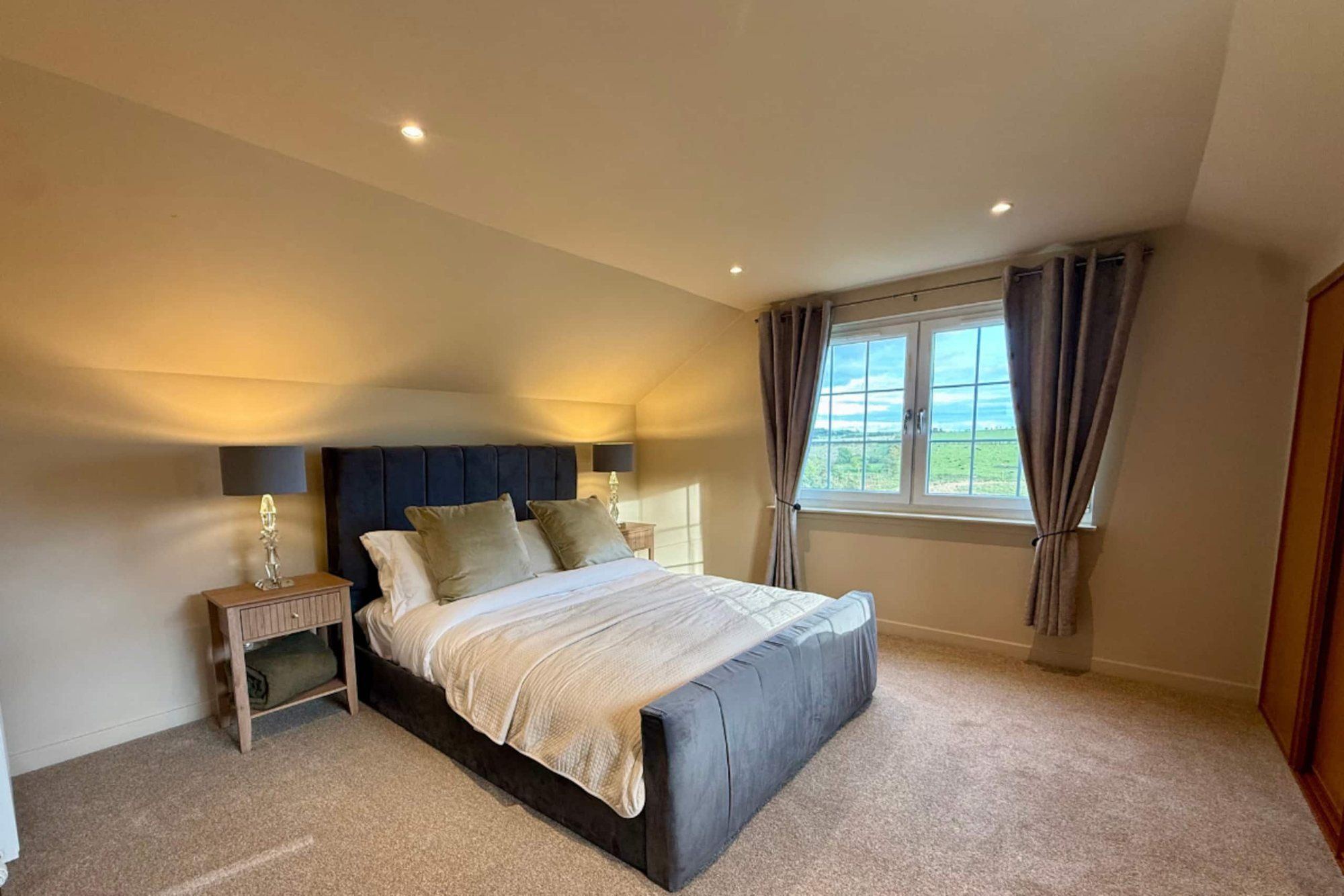 King bedroom at Cranley Cottage with a padded headboard, bedside lamps and a window onto the fields