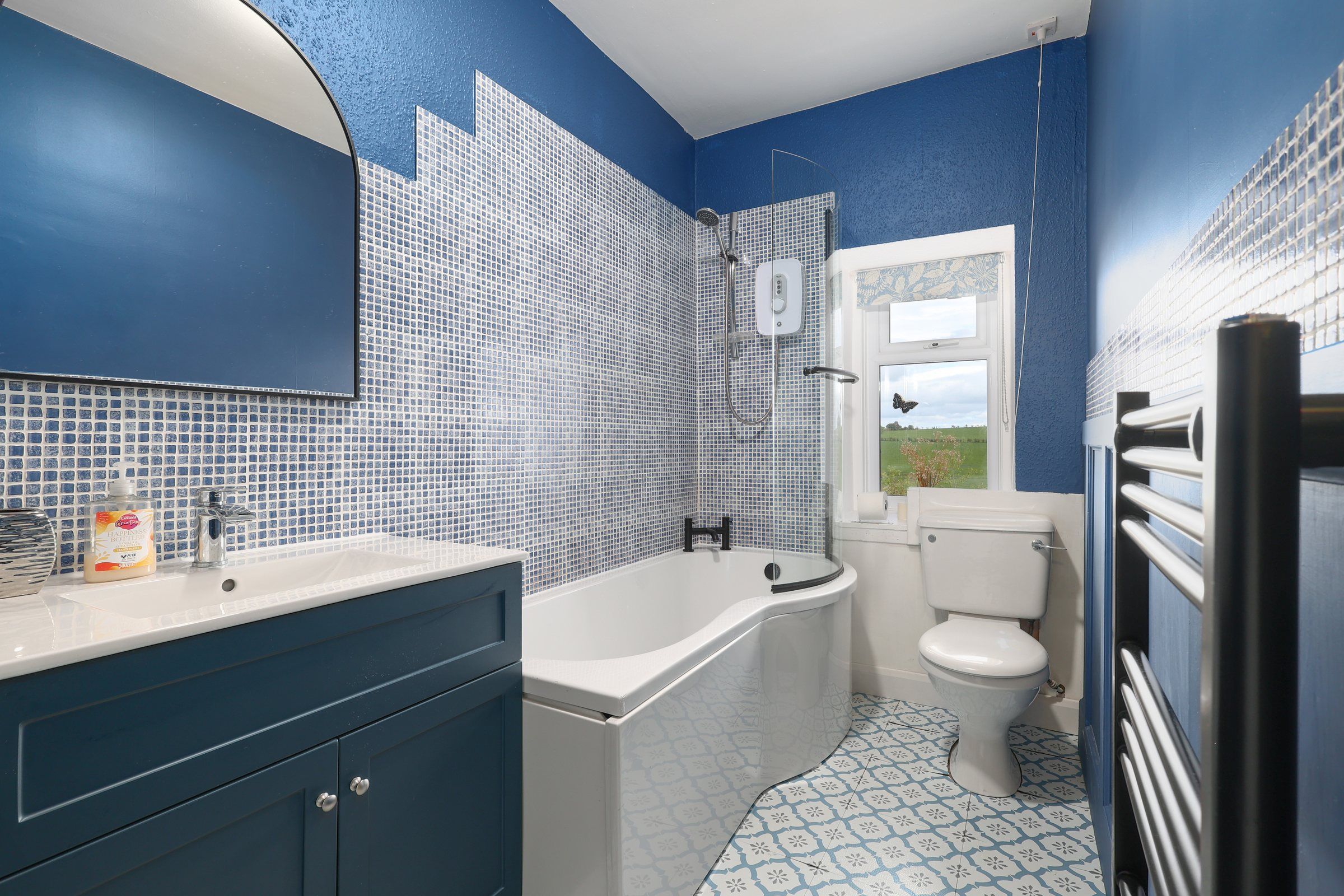 Blue bathroom at Gardener's Cottage with mosaic tiles, a shower over the bath and patterned floor tiles
