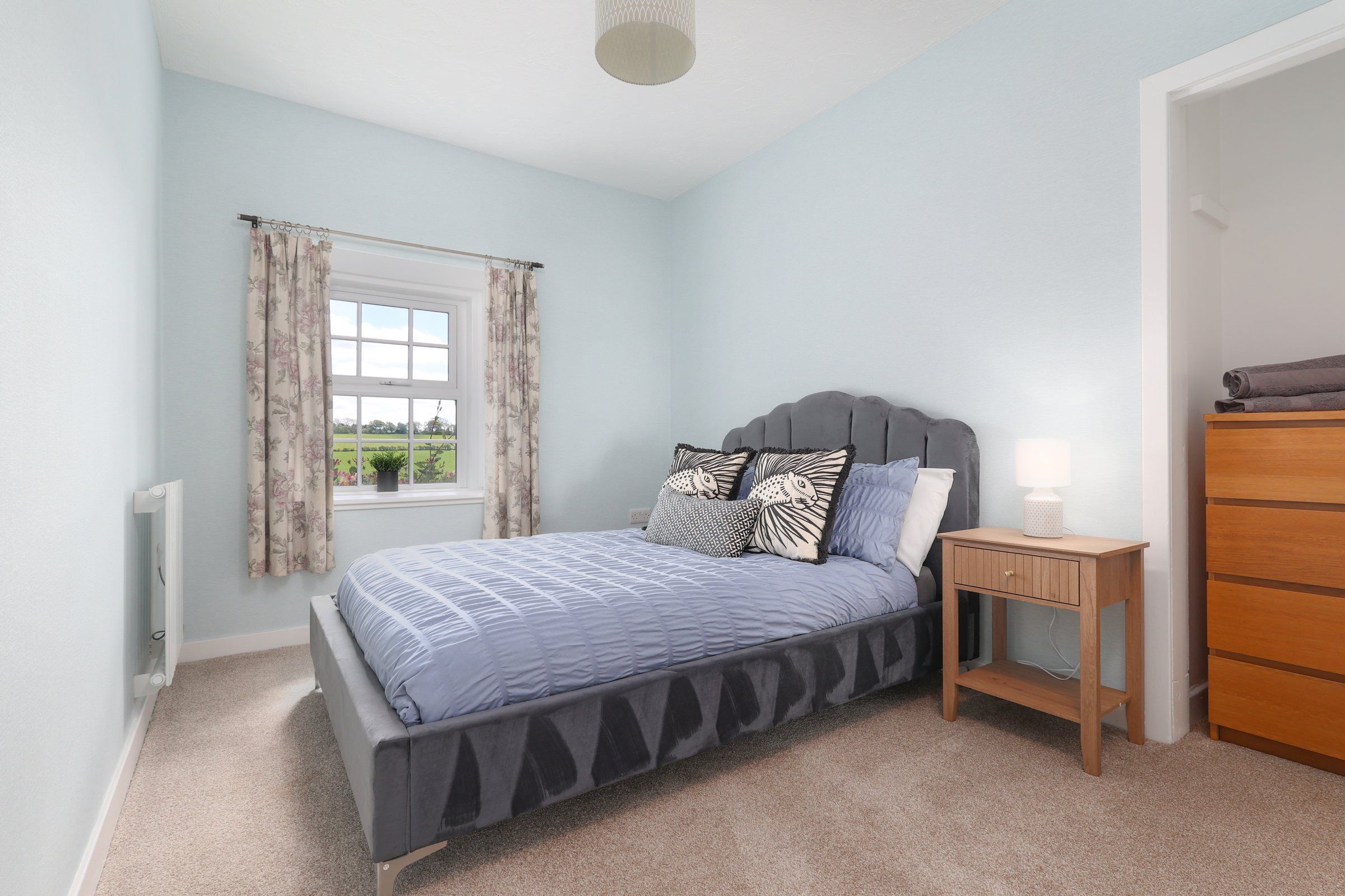 Second double bedroom with a scalloped velvet headboard, soft blue bedding and a window onto the fields