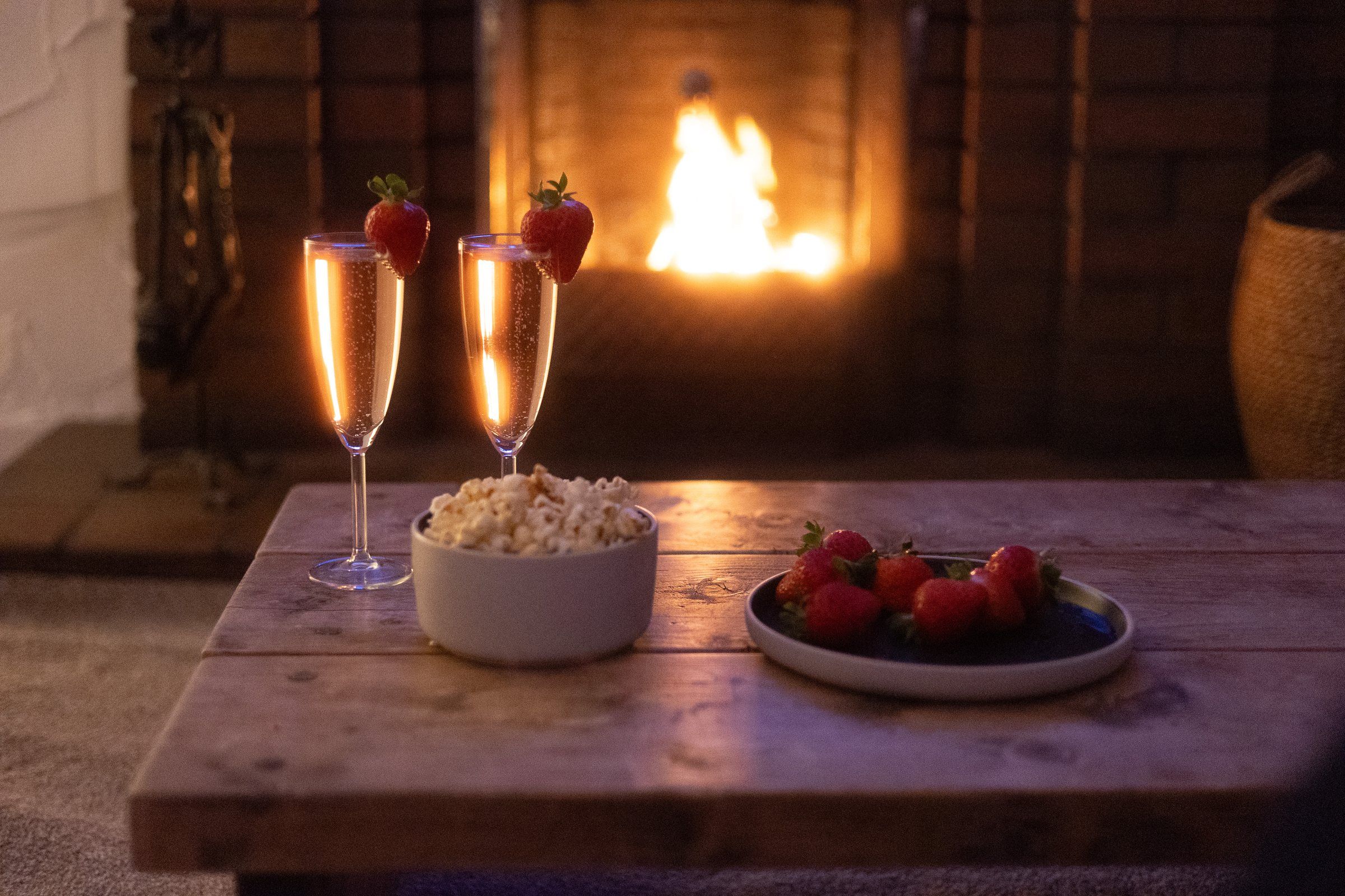 Two glasses of fizz, strawberries and popcorn on the coffee table in front of the fire