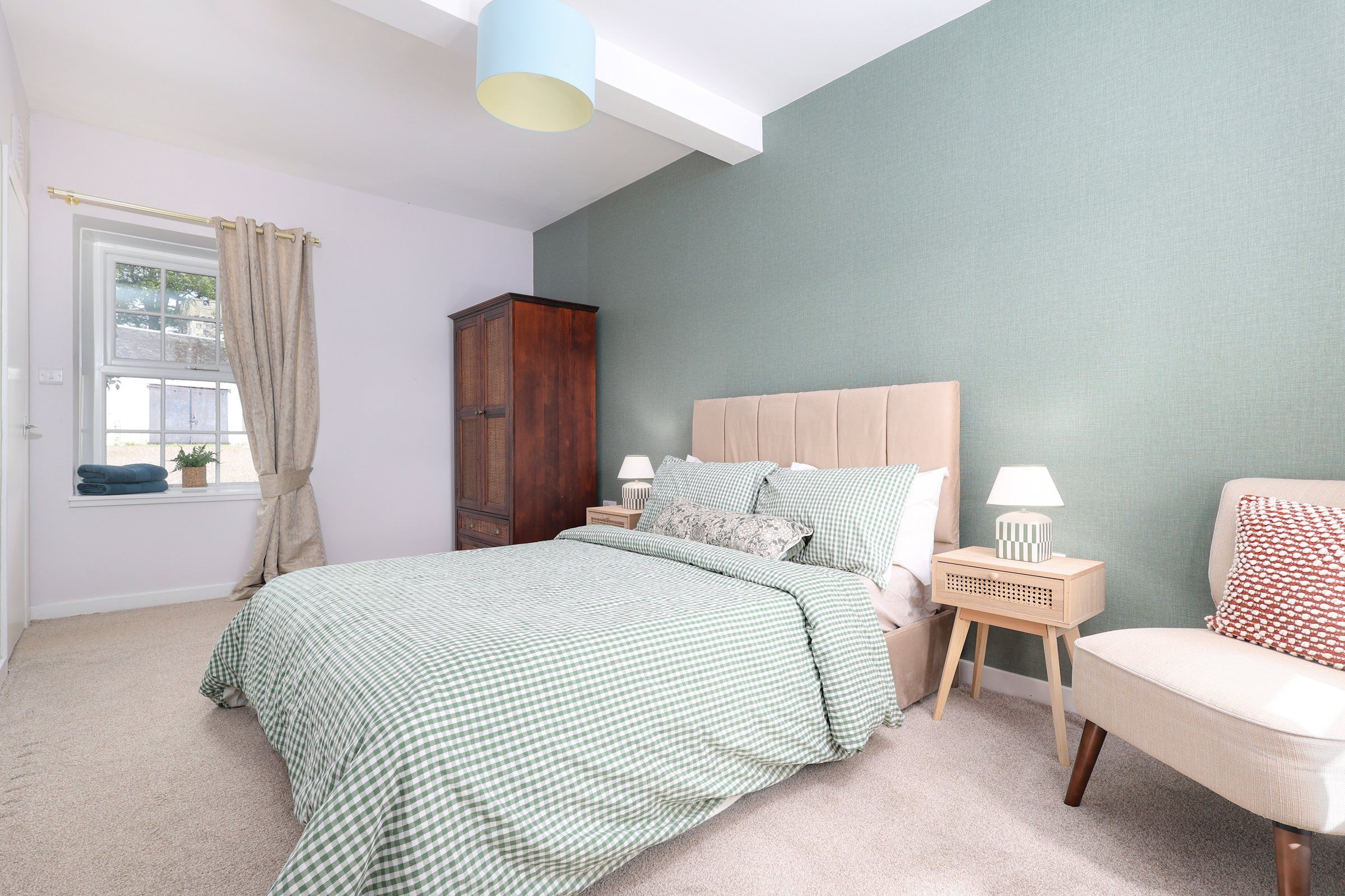 Double bedroom with green gingham bedding, a velvet headboard and a cane wardrobe