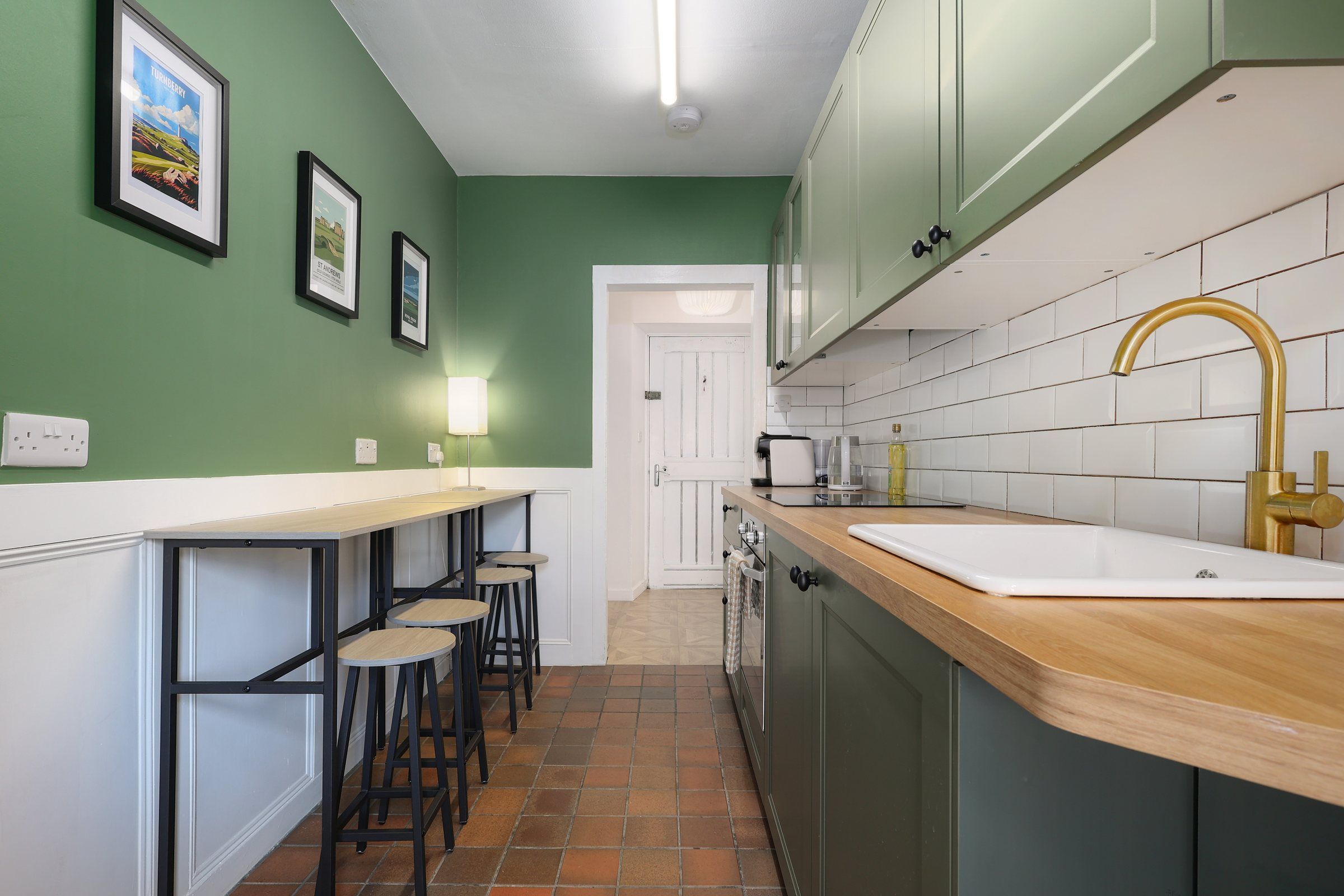Green shaker kitchen at Gardener's Cottage with oak worktops, a brass tap and a breakfast bar with stools