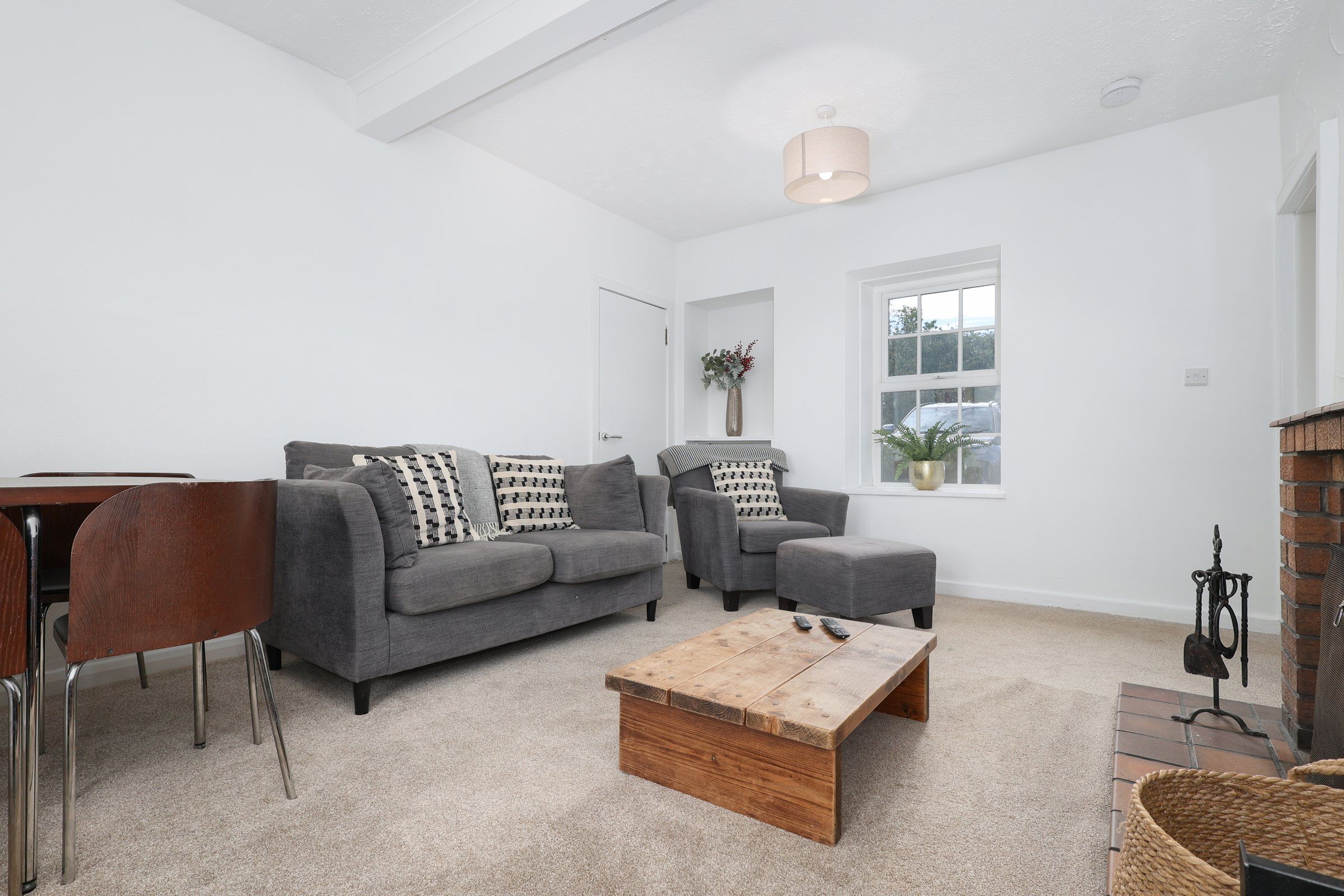 Bright living room at Gardener's Cottage with grey sofas, a rustic timber coffee table and a window onto the fields